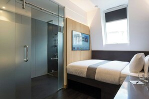 A modern hotel room with a bed, a TV mounted on the wall, a glass door closet, and a window. - Z Tottenham Court Road (London)