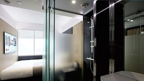 A modern hotel room with a bed, a glass shower enclosure, and a mounted TV displaying various channels. - Z Tottenham Court Road (London)