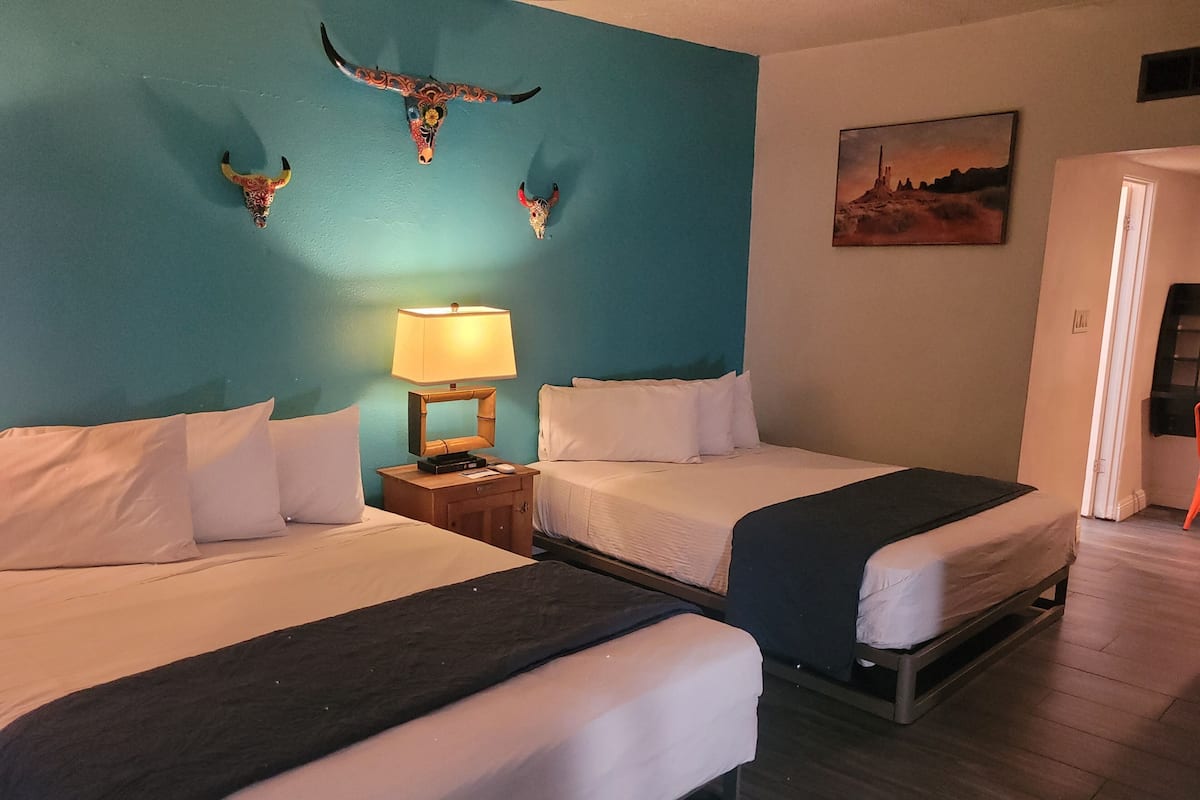 A hotel room with two beds, a nightstand with a lamp, and decorative wall art.