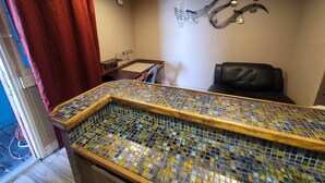 Una habitación con una barra revestida con azulejos, un sillón de cuero negro y una lámpara de pared.