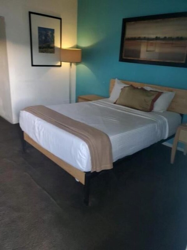 A neatly made bed with a white and beige bedspread, a wooden headboard, and a nightstand with a lamp.