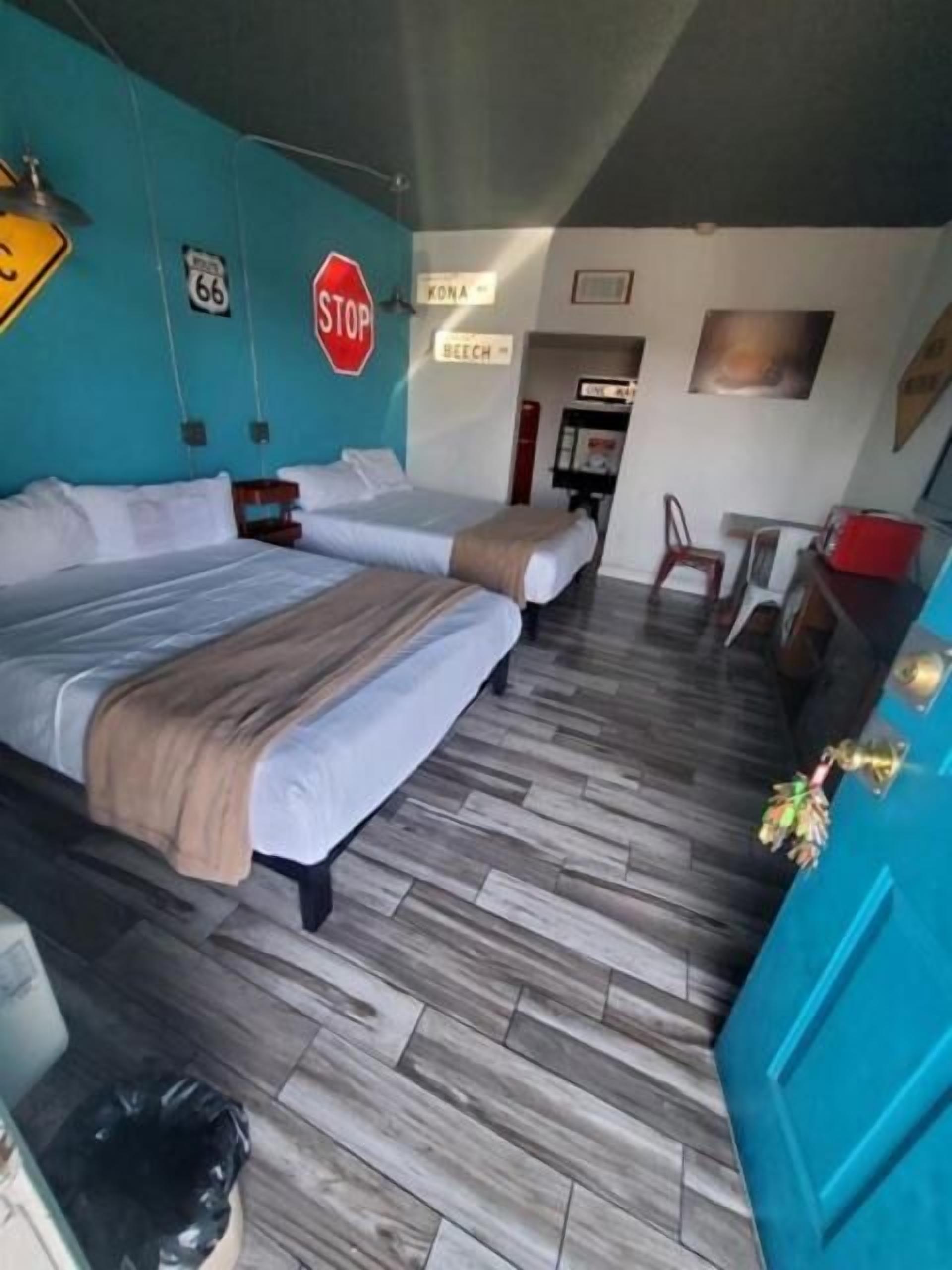 A hotel room with two beds, a blue wall, a stop sign, and a sign that says "KONA."