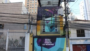 A building with a colorful mural advertising 'BISTRO HOSTEL EVENTOS CO WORKING'. - Hacker Hostel (São Paulo)