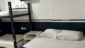 A bunk bed room with a blue bedspread, white pillows, and a small shelf above the upper bunk. - Hacker Hostel (São Paulo)
