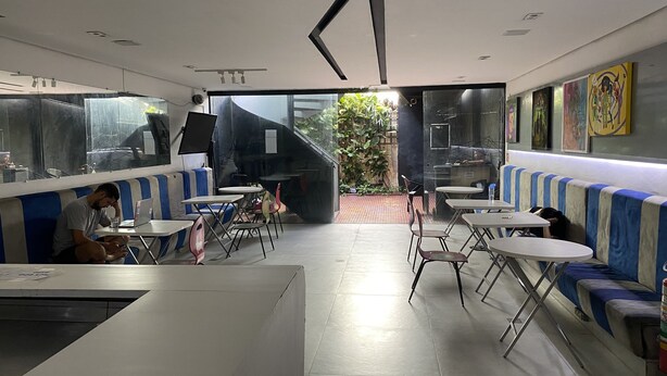 A modern cafe with high tables and booths, large windows, and artwork on the walls. - Hacker Hostel (São Paulo)
