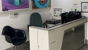 A reception desk with artwork on the walls, a black office chair, and a tiled floor. - Hacker Hostel (São Paulo)