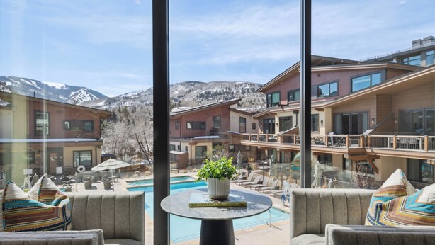A modern hotel room with a large window overlooking a pool and mountains. - One Riverfront Village by EWH (Avon)
