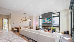 A modern living room with a marble countertop, a large sofa, a fireplace, and a television mounted on the wall. - One Riverfront Village by EWH (Avon)