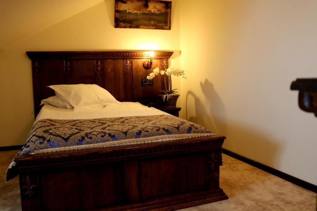 Ein traditionelles hölzernes Bett mit einem gemusterten Überwurf, ein Nachttisch mit Blumen und ein Bild über dem Bett.