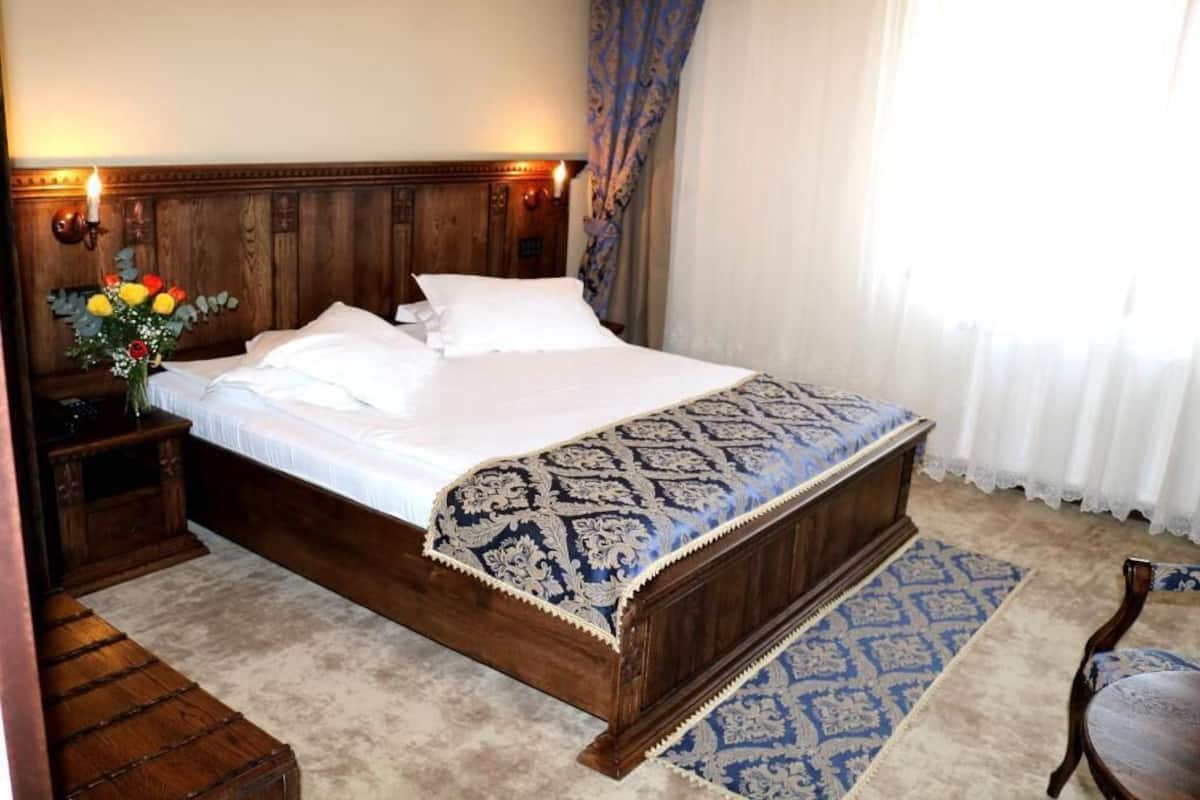 A neatly made bed with a patterned bedspread, a wooden headboard, and a nightstand with a vase of flowers.