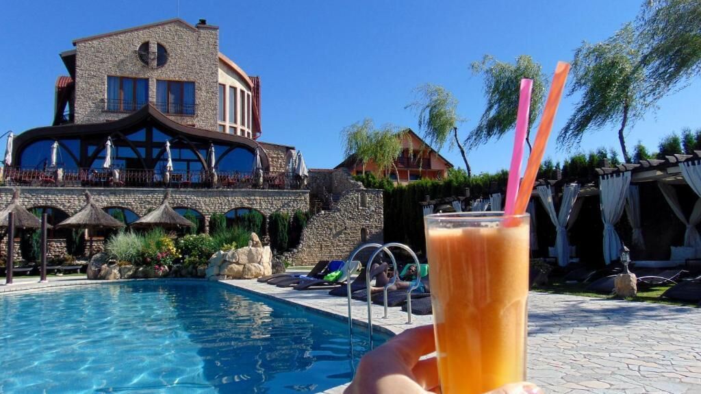 A swimming pool with lounge chairs and umbrellas, a stone building with a balcony, and a clear blue sky.