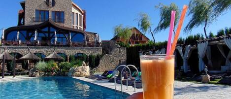 A swimming pool with lounge chairs and umbrellas, a stone building with a balcony, and a clear blue sky.