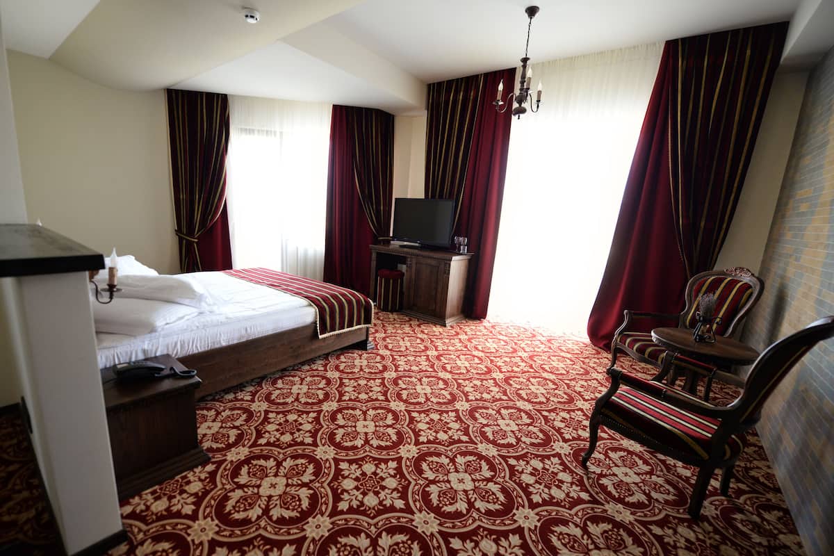 A hotel room with a bed, a desk with a television, a chair, and a carpeted floor.
