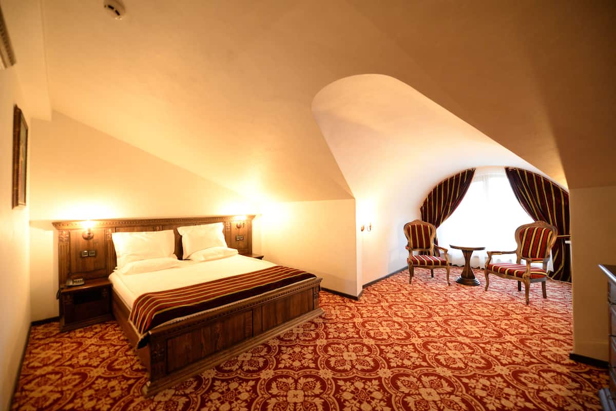 A bedroom with a large bed, a wooden nightstand, a chair, a small table, and a curved ceiling.