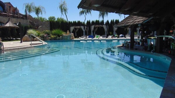 Piscina con sillas de descanso y sombrillas, rodeada por un muro de piedra y vegetación.