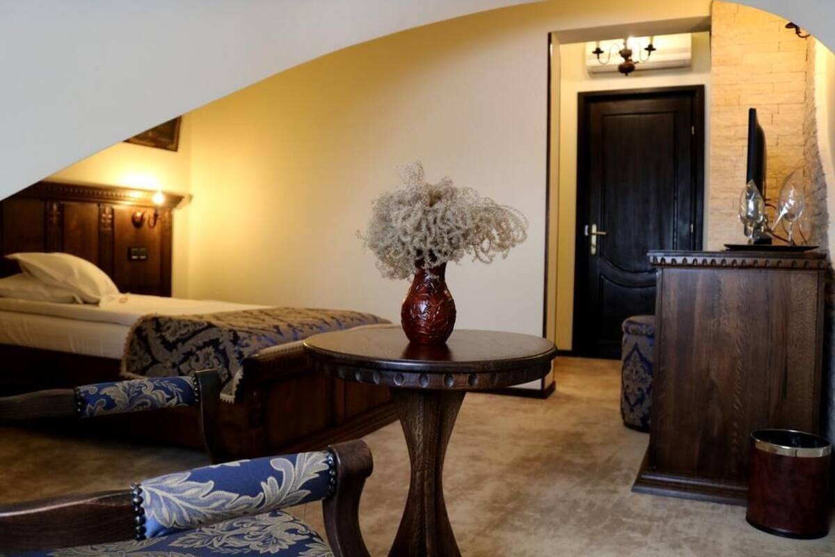 A hotel room with a bed, a round table with a vase, a wooden cabinet, and a door.