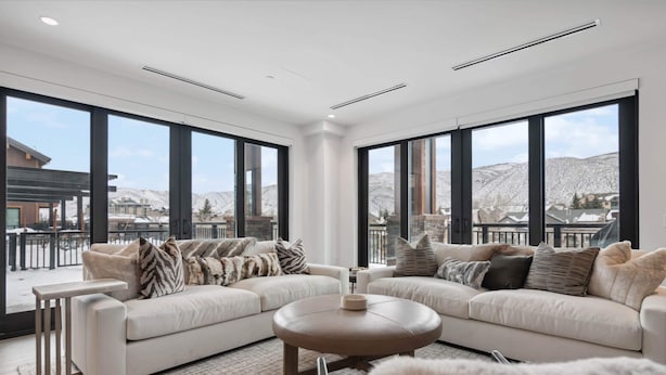 Ein geräumiges Wohnzimmer mit einer großen Eckcouch, einem runden Couchtisch und Blick auf eine verschneite Berglandschaft durch große Fenster.