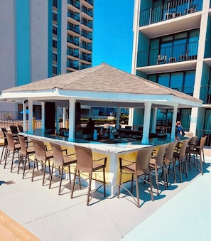 A covered outdoor bar area with a pool table, bar stools, and a pool. - Deluxe Ocean Front 1 bdrm, sleeps 8, pools, lazy river, hot tubs, tiki bar (Myrtle Beach)