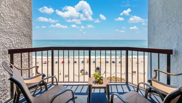 A balcony with a view of a beach, featuring a table with a frog decoration and a potted plant. - Oceanfront one bedroom deluxe, sleeps up to 8 ppl 20+pools, lazy river,hot tubs (Myrtle Beach)