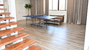 A spacious room with a ping pong table, a brown leather couch, and a staircase. - Modern cozy home, pet friendly (Wolcott)