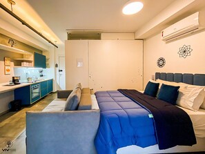A compact hotel room with a kitchenette, a bed with blue bedding, and a ceiling light. - Sky Visiom (São Paulo)