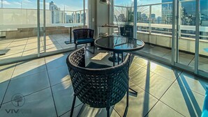 Un balcon spacieux avec une table ronde en verre et deux fauteuils en osier, offrant une vue sur la ville.