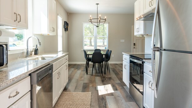 A modern kitchen with white cabinets, stainless steel appliances, and a dining area with a chandelier. - NEW! Duke~King Bed~Speakeasy Hideout (Durham)