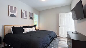 A bedroom with a bed, a dresser, a TV, and artwork on the wall. - NEW! Duke~King Bed~Speakeasy Hideout (Durham)