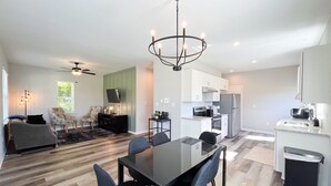A modern kitchen with white cabinets, a stainless steel refrigerator, and a dining area with a glass table and chairs. - NEW! Duke~King Bed~Speakeasy Hideout (Durham)