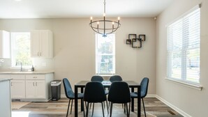 A dining area with a chandelier, a window with blinds, and a view of the outside. - NEW! Duke~King Bed~Speakeasy Hideout (Durham)
