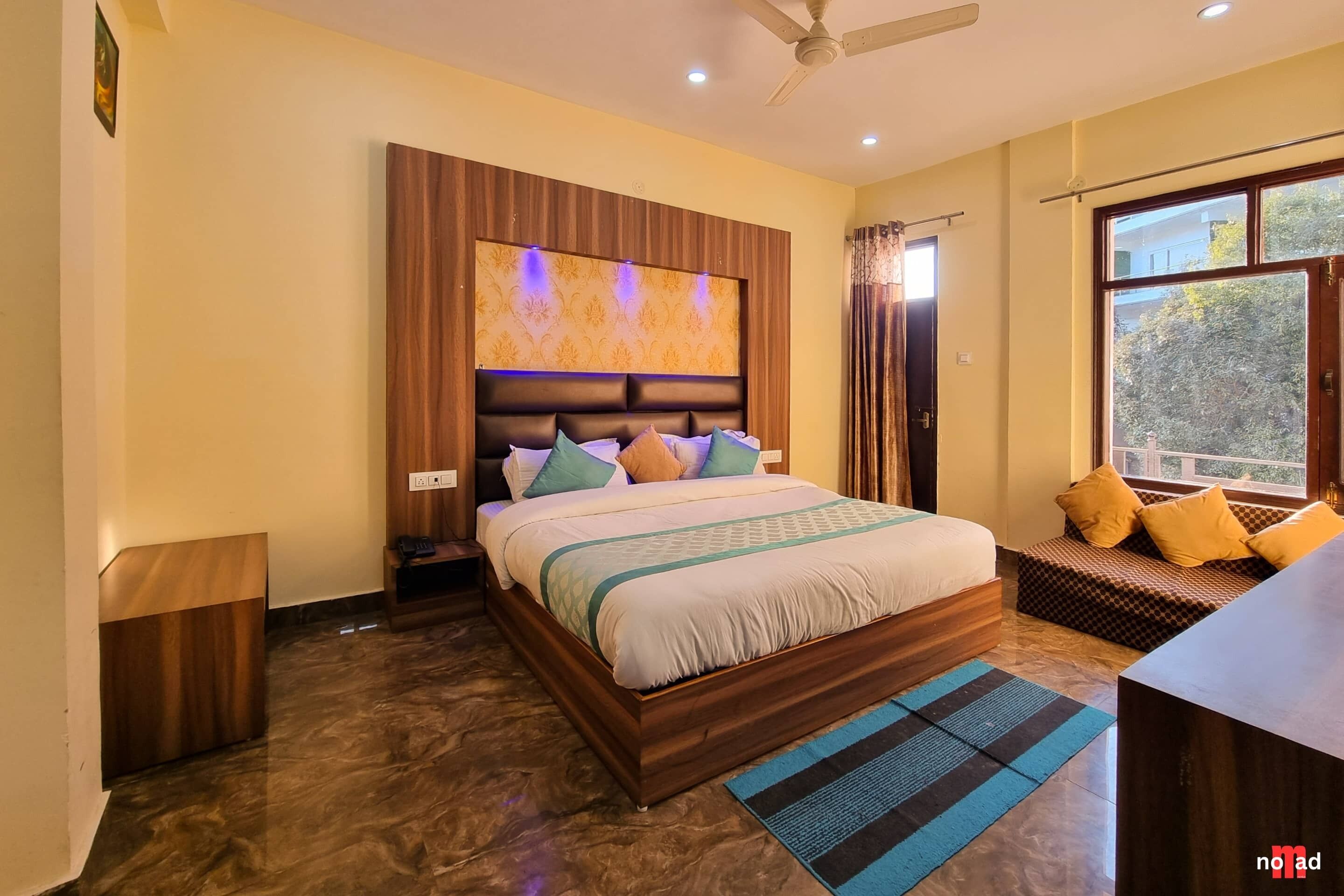 A bedroom with a wooden bed, a nightstand, a desk, a window with curtains, and a ceiling fan.