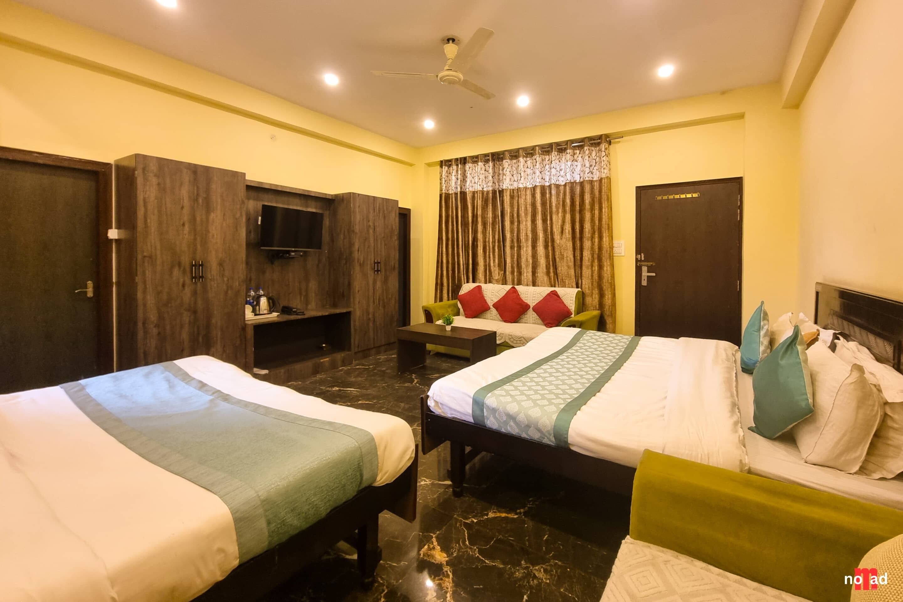 Habitación de hotel con dos camas, televisor, ventilador de techo y ventana con cortinas.