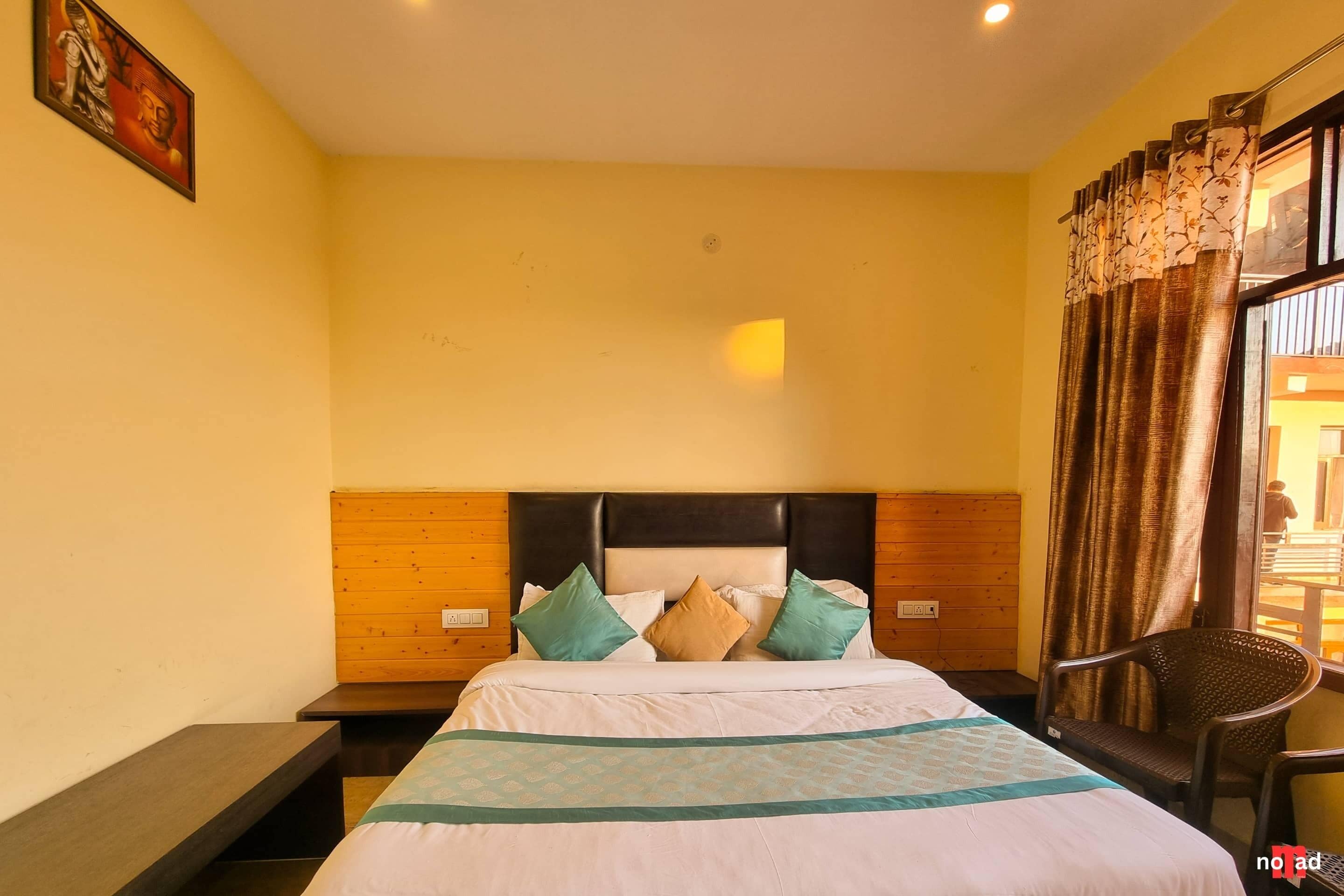 Una habitación de hotel con cabecera de madera, cama con edredón estampado y una silla cerca de la ventana.