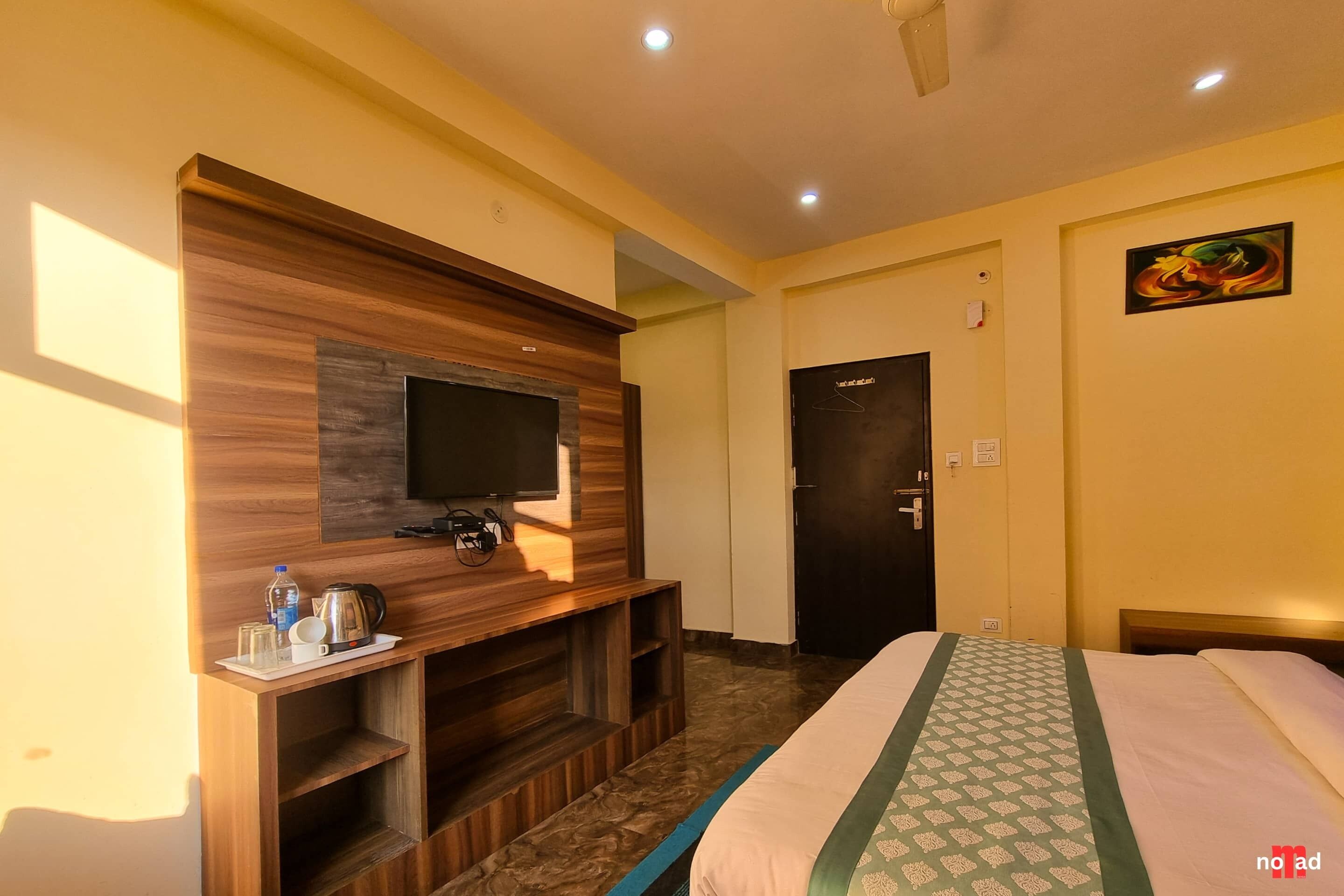 Quarto de hotel com uma cama, uma televisão fixada numa parede de madeira, uma porta e um quadro na parede.