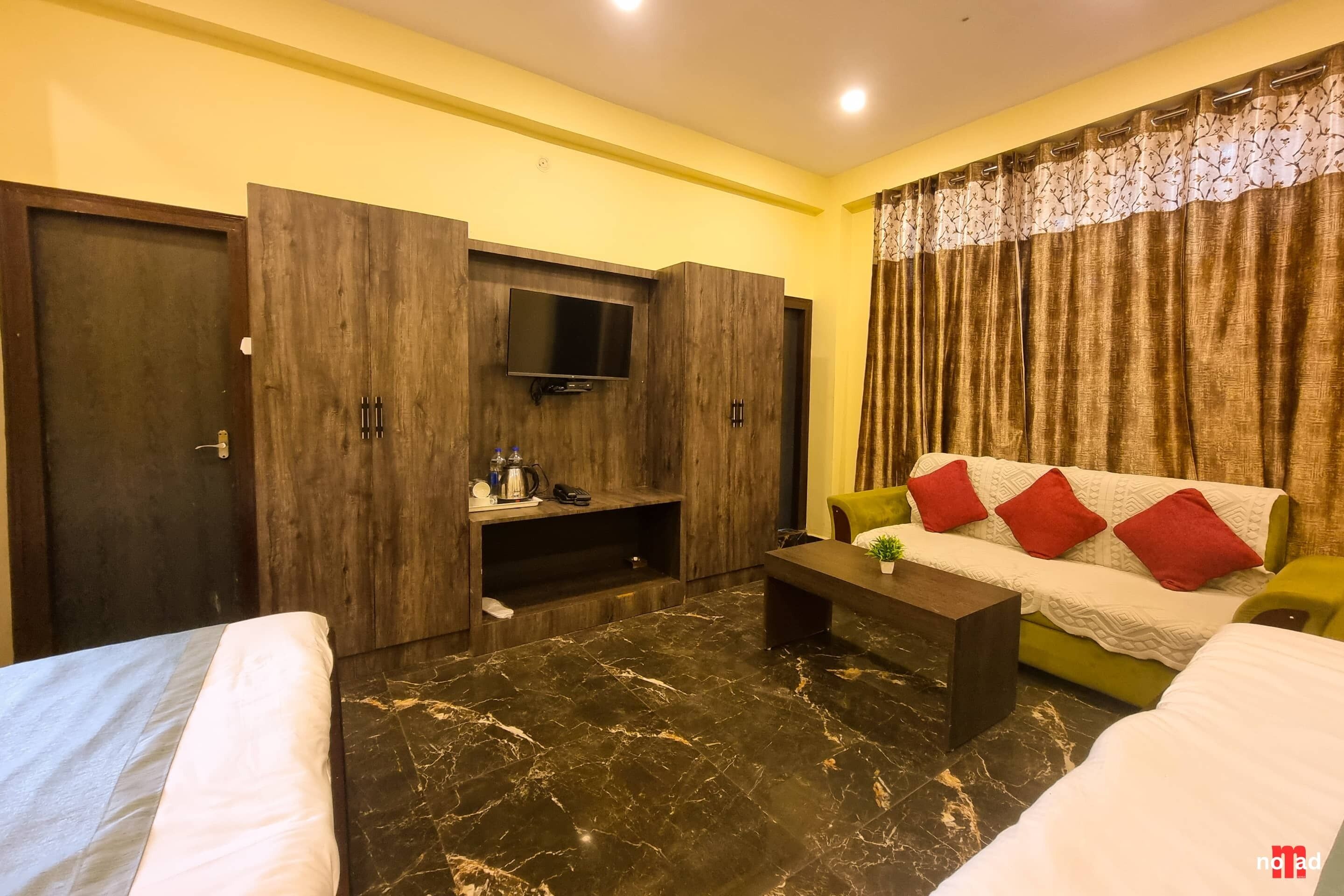 A hotel room with a bed, a sofa, a TV mounted on a wooden wall, and a coffee table.