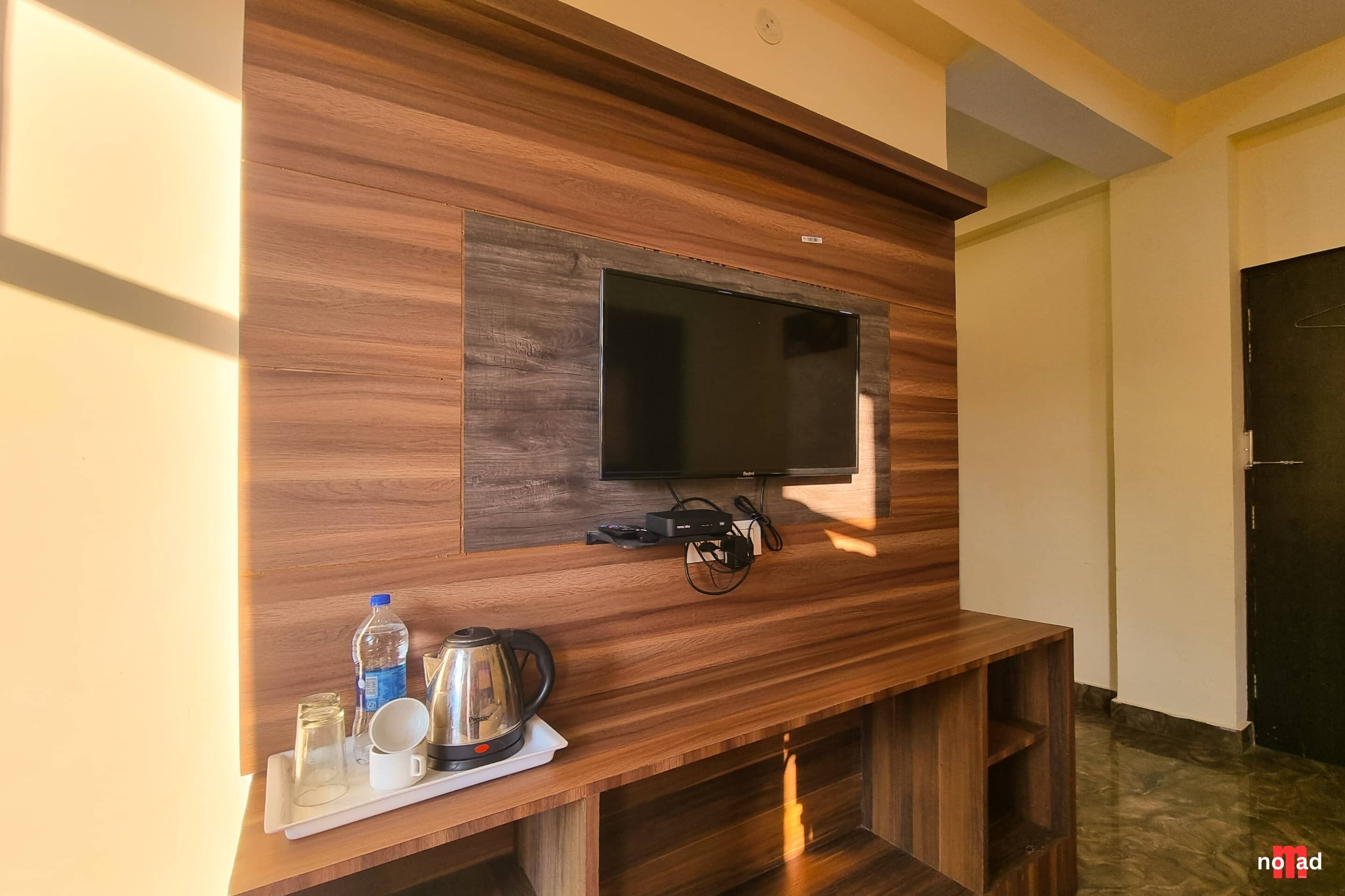 Una sala de estar moderna con un televisor de pantalla plana montado en una pared de madera, una mesa de centro con un hervidor, tazas y una botella de agua.