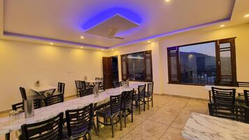 A dining area with multiple tables and chairs, a ceiling fan, and large windows with a view.