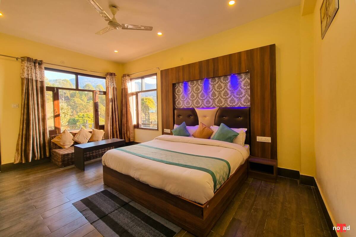 A bedroom with a large bed, a bench, and a view of trees through the window.
