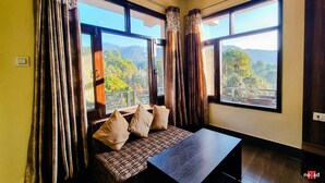 A room with a bed, a table, and large windows offering a mountain view. - Nature Nest By Nomad Hotels (Dalhousie)