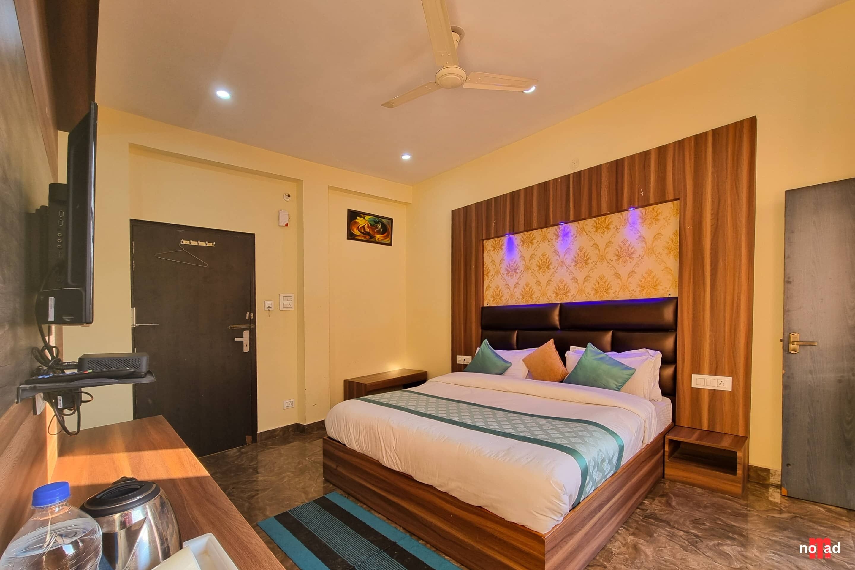 A hotel room with a bed, a TV, a desk with a kettle, and a door.