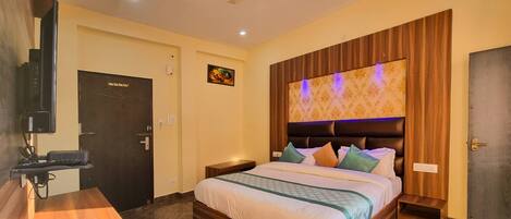 A hotel room with a bed, a TV, a desk with a kettle, and a door.