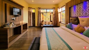 A hotel room with a bed, a TV mounted on the wall, a desk with a kettle, and a view of trees through the window. - Nature Nest By Nomad Hotels (Dalhousie)