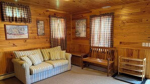 Et hyggeligt sommerhusinteriør med en stribet sofa, en træstol og ternede gardiner.