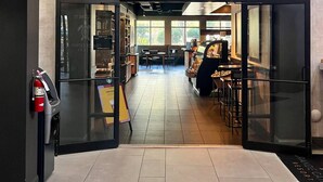 Der Eingang eines Starbucks mit modernem Design, inklusive Glastür, Feuerlöscher und sichtbarem Sitzbereich im Inneren.
