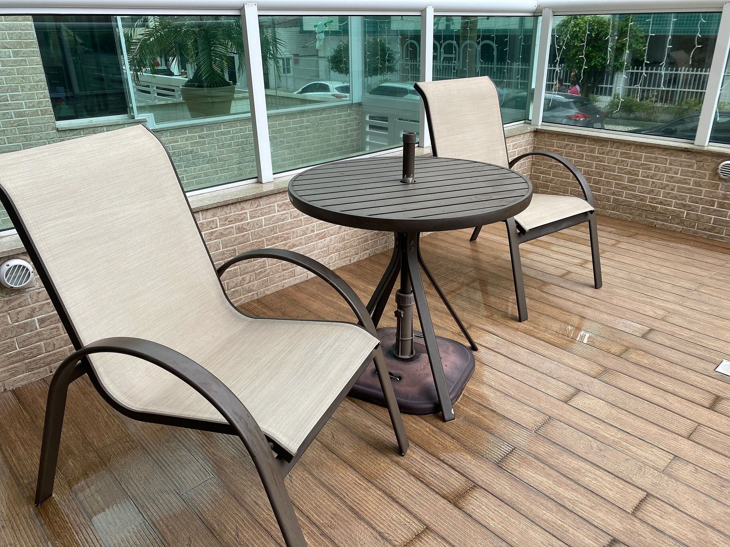 A patio area with a round table and two chairs, a brick wall, and a window overlooking a street.