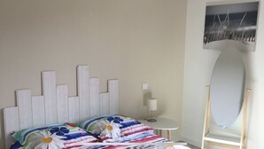 A bedroom with a bed, a small table, a chair, and a wall-mounted mirror.