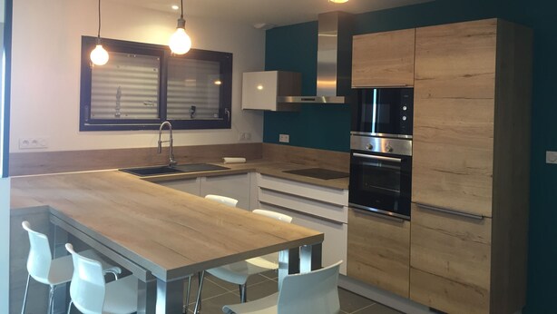 A modern kitchen with a wooden table, white chairs, a built-in oven, and a window with blinds.