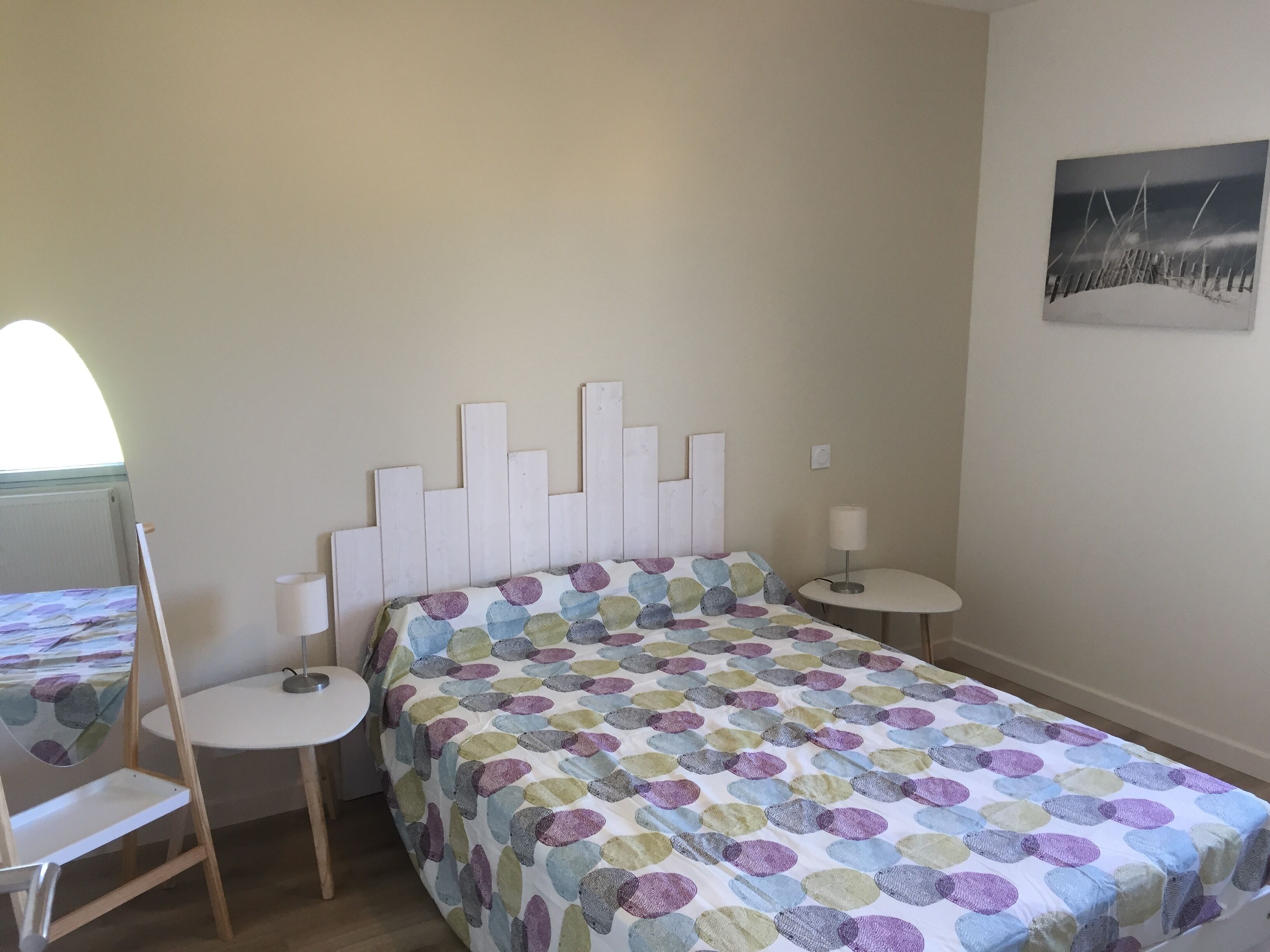 A bedroom with a bed, two bedside tables, a chair, a window, and a wall-mounted picture.