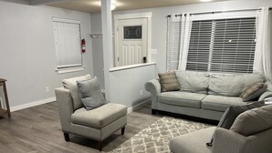 Una sala de estar con un sofá gris, un sillón gris y una alfombra estampada.