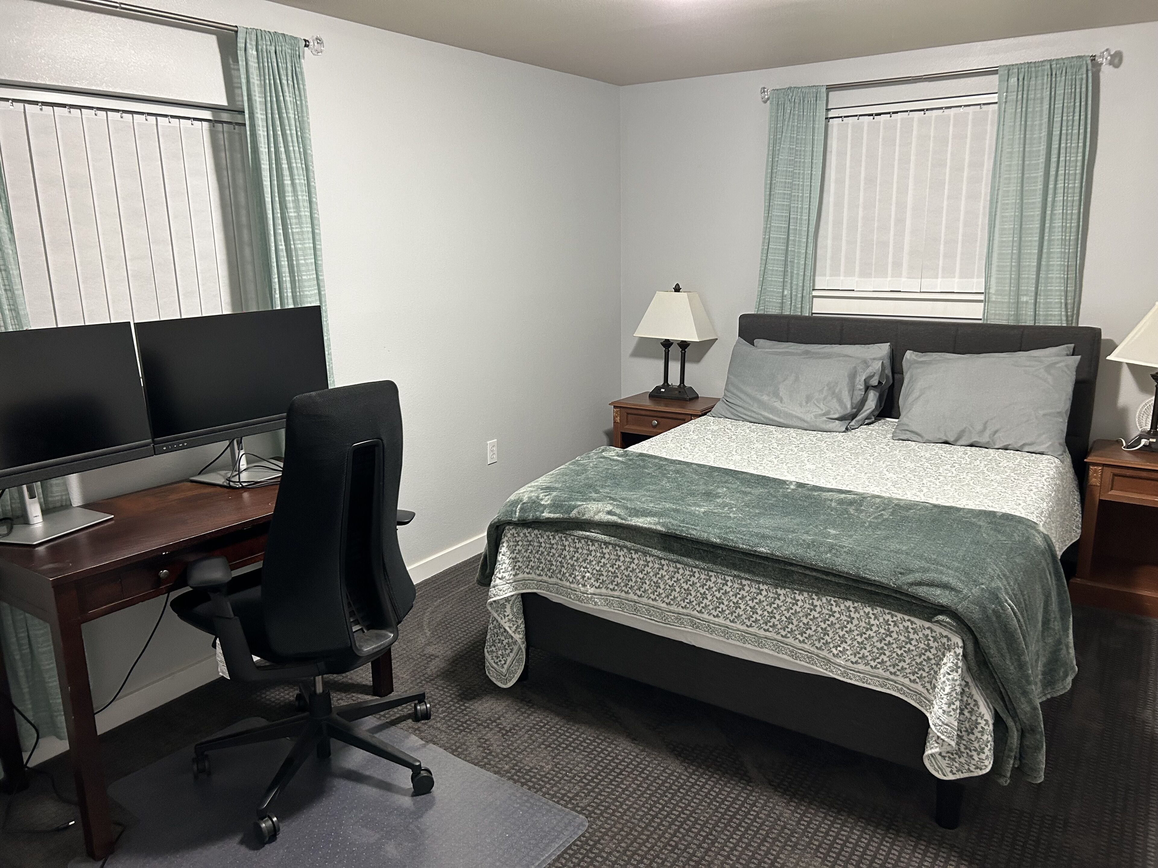 A bedroom with a bed, a desk with a computer, a chair, and two bedside lamps.